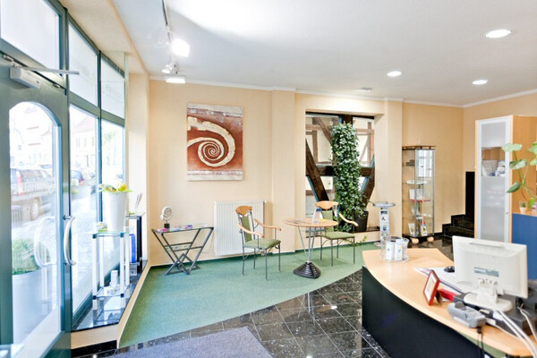 Heller Empfangsbereich einer modernen Arztpraxis mit Wartebereich und Dekoration.